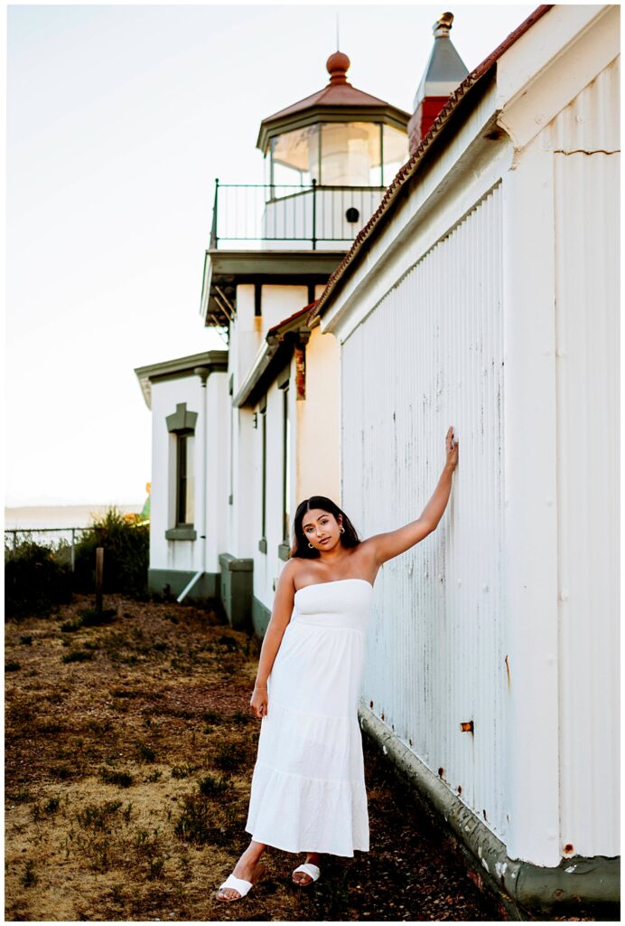 Seattle senior girl leaning on the lighthouse at Discovery Park in Seattle Washington, wearing a white dress, Seattle Summer Senior Portraits