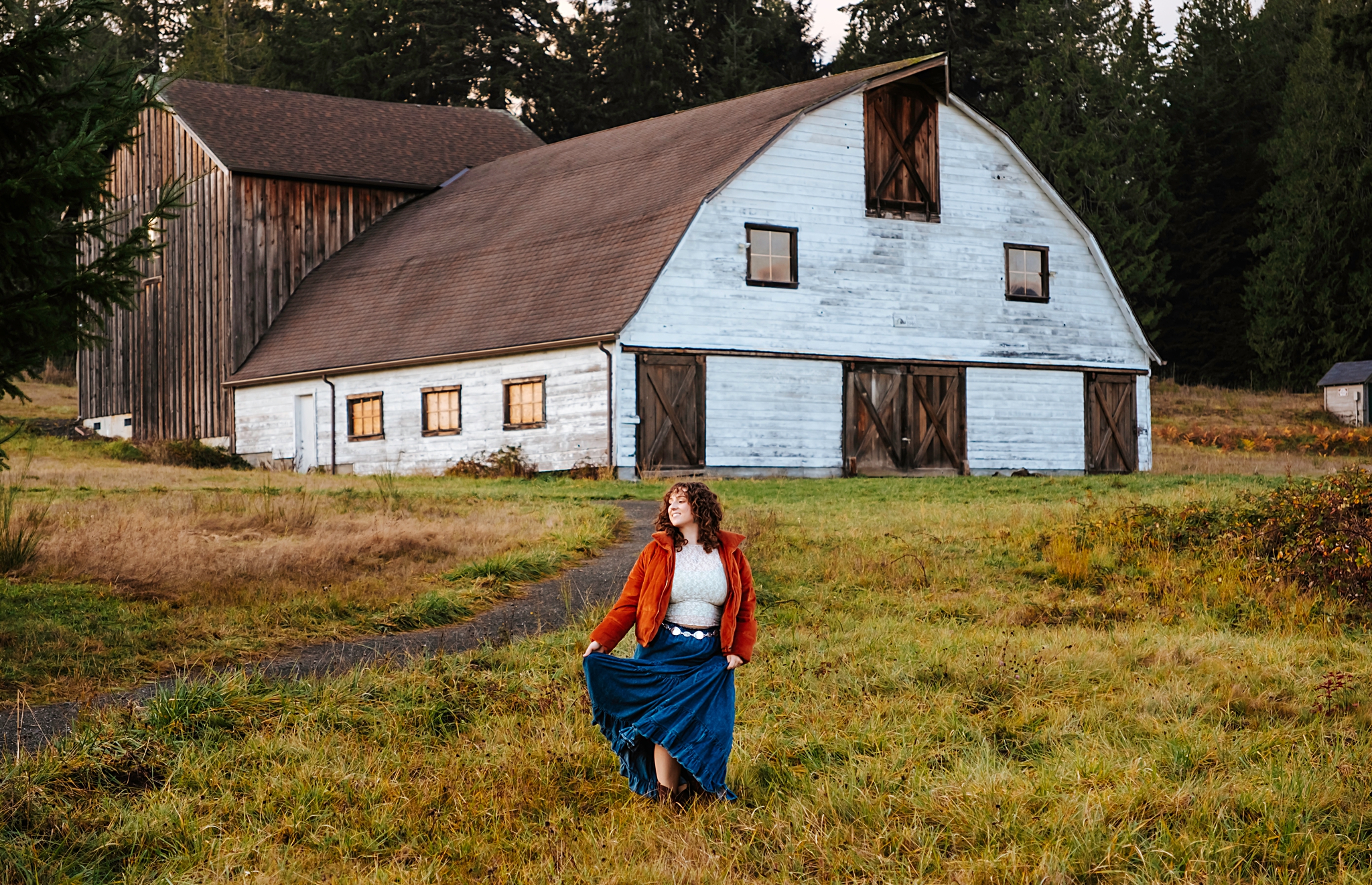 The model is holding her skirt and looking to the side, standing in front of a barn at Howe Farm Park in Port Orchard, WA